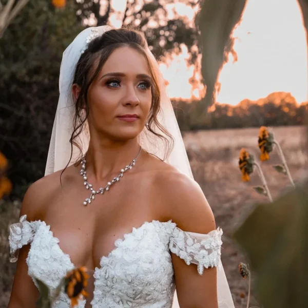 Bride with a soft updo, veil and statement necklace in a sunflower field, hair by Chair'istry Salon