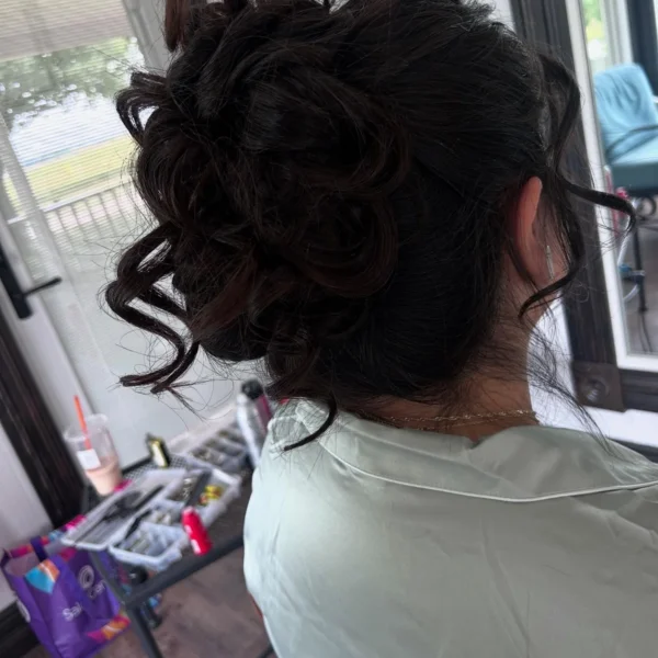 Back view of a voluminous dark curly updo with loose face-framing tendrils by Chair'istry Salon