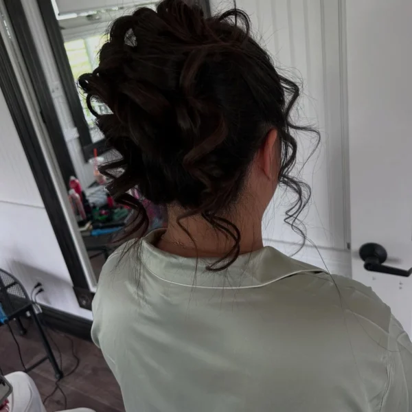 Side view of a pinned dark curly updo with loose curls at the neckline, styled at Chair'istry Salon