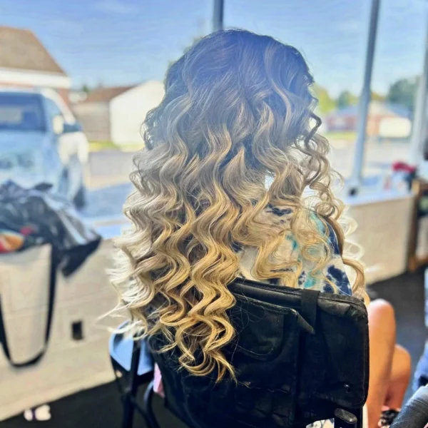 Long curled hair blending from dark roots into bright blonde ends, styled at Chair'istry Salon in Wichita