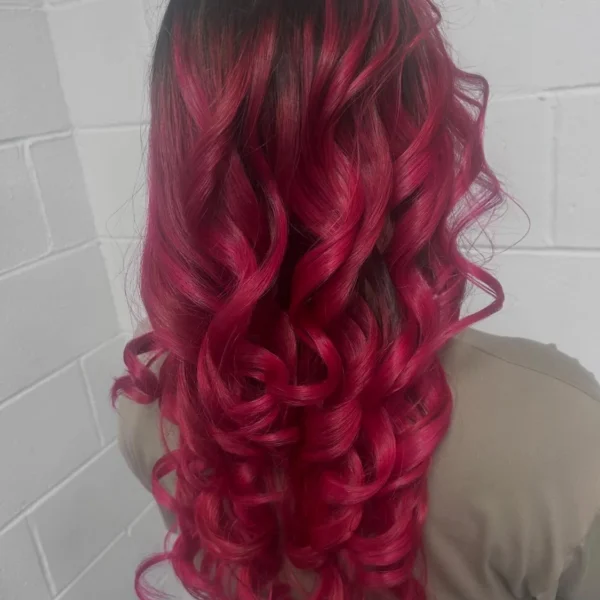 Long hair colored from dark roots into vibrant red ombre and styled in loose curls at Chair'istry Salon